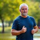 Uomo italiano di circa 50 anni, energico e vitale, in una posa dinamica durante una passeggiata all'aria aperta, la luce del mattino lo illumina, simboleggiando un aumento di energia e perdita di peso.